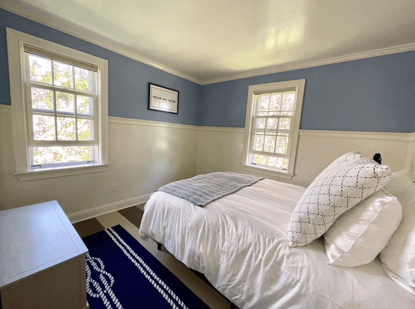Blue bedroom with twin windows and a nautical rug